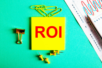 Fototapete - ROI Return On Investment is written in red on a yellow sticker on a green background near the graph and pencil