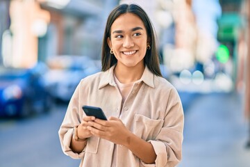 Poster - Young latin girl smiling happy using smartphone at the city.