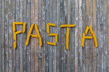 The Word Pasta Written Using Penne Against A Grey Wooden Background 