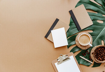 A simple trendy office Desk. Coffee cup, monstera leaf, blank card and notebook .Home Office desktop with space copying. Top view, copy space. Minimal concept