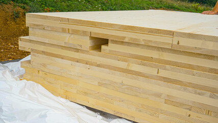 CLOSE UP: A stack of CLT wall panels lie uncovered at a construction site.