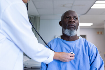 Caucasian female doctor examining with stethoscope african american male patient in hospital room