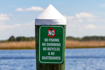 Sign on a dock post by the sea says no swimming, diving, cycling or skateboarding on the pier. Versatile image with health and safety or  restricitive regulations limiting freedom concepts.