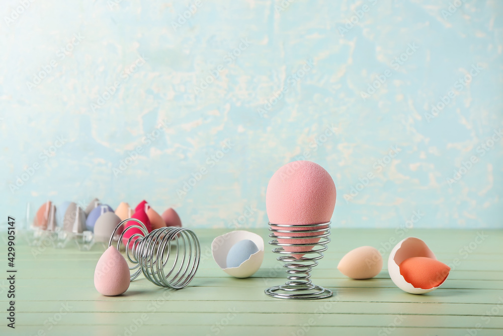 Creative composition with makeup sponges and eggs holders on table against color background
