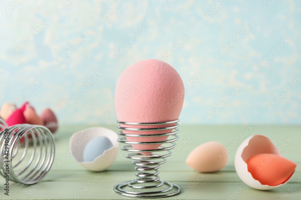 Creative composition with makeup sponges and eggs holders on table against color background, closeup