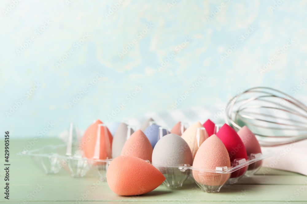 Plastic egg holder with makeup sponges on color background