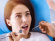 © rogerphoto - Smiling brunette woman being examined by dentist at sunny dental clinic. Hands of a doctor holding dental instruments near patient's mouth. Healthy teeth and medicine concept