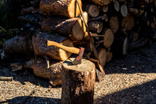 One-handed Axe Stuck In Pine Log With Two-handed Axe And Firewood Piled On The Bottom
