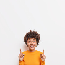 Photo Of Cheerful African American Female Points Fingers Up At Top Promo Text Suggests To Check Out Awesome Offer Demonstrates Copy Space Banner Against White Background Wears Casual Jumper.