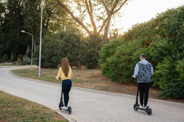  A young beautiful couple rides electric scooters in the Park on a warm autumn day. Hobbies and recreation.
