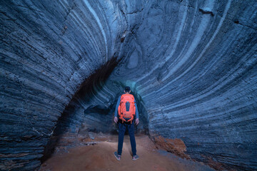 Back of tourist man travelling in blue cave with rocks, Mae Sot District, Tak, Thailand. Cave wall pattern with natural landscape. Tourist attraction landmark. Adventure activity. Backpacker people.