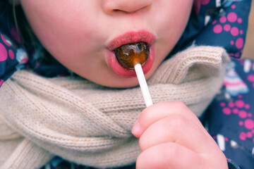 Close up of face young cute little girl in warm autumn clothes  tasting a lollypop outdoors