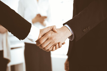 Businessman and woman shaking hands with colleagues at the background. Handshake at meeting in office. Concept of success in business