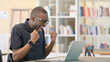 © stockbakers - Ambitious African Man Celebrating Success on Laptop in Library