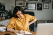 © Oleksandr - Smiling business woman talking on a mobile phone and using a laptop while working at home, looking at the screen, reading a message, a young female employee advises a client, telephone conversations