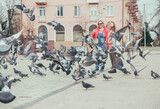 Fototapeta  - Mom and daughter feed pigeons on the street