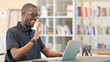 © stockbakers - Cheerful Young African Man doing Video Chat on Laptop in Library