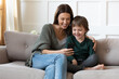 © fizkes - Happy young mom and small 7s son relax on sofa in living room have fun use browse cellphone together. Smiling Caucasian mother and little boy child have webcam digital video call on smartphone.