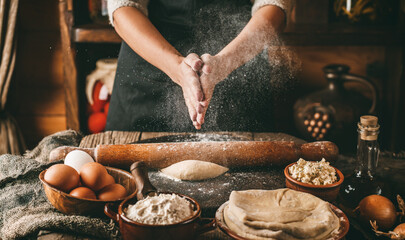 Woman hands cooking dough on rustic wooden background. White flour flying into air. Cooking bread with cheese, eggs and herb. Homemade healthy food concept, toning