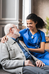 Vertical photo of helpful young female doctor nurse consulting old elderly man . 80s senior man talking about health condition and medicine with woman general practitioner.