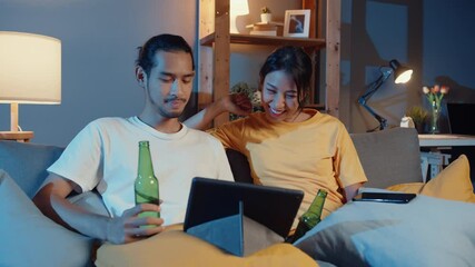 Sticker - Happy young asian couple enjoy night party event online sit couch use tablet video call with friends toast drink beer via video call online in living room at home, Social distancing concept.