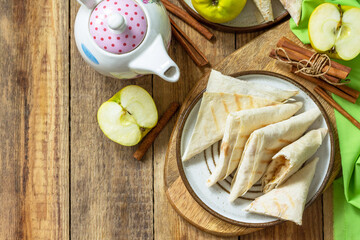 Wall Mural - Apple pastries for breakfast. Grilled lavash triangle with apples and cinnamon on a wooden wooden table. Top view, flat lay. Copy space.