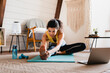 © InsideCreativeHouse - Young fit sporty afro woman doing stretching exercises indoors. Black fitness woman exercising at laptop having online training at home. Stay fit concept