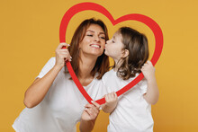 Happy Woman In Basic White T-shirt Have Fun With Child Baby Girl 5-6 Years Old Hold Heart. Mom Little Kid Daughter Isolated On Yellow Orange Color Background Studio. Mother's Day Love Family Concept.