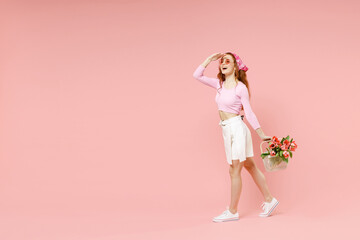 Poster - Full length side view young woman 20s in rose clothes bandana glasses hold tulips flowers bouquet hold hand at forehead look far away distance isolated on pastel pink background Spring season concept.