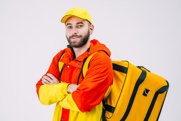 Delivery service concept. of a confident smiling courier wearing a red yellow uniform and a thermal backpack posing with crossed arms and looking at the camera.