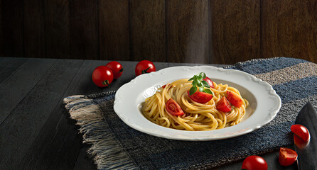 Plate with spaghetti, tomatoes and basil on a dark wood background. Hot spaghetti with steam. Copy Space