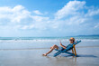 © CandyRetriever  - Asian man resting on sunbed on tropical beach. Happy guy sitting on beach chair by the sea using smartphone for selfie or video call. Handsome male enjoy beach outdoor lifestyle on summer vacation