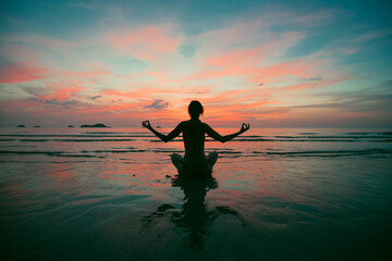 Wall Mural - A woman practicing yoga on the beach during surreal sunset.