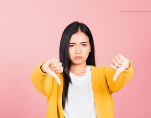 Wall Mural - Portrait Asian beautiful young woman unhappy, negative gesture showing finger thumbs down or dislike sign, studio shot isolated on pink background, Thai female rejection unlike with copy space