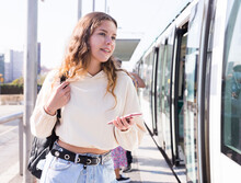 Active Confident Girl With A Mobile Phone In Her Hands At The Bus Stop Is Going To Enter The Tram To Go On Business