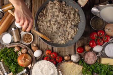 Wall Mural - Chef fries chicken fillet in a skillet. Top view on an old wooden table with ingredients. Culinary recipes
