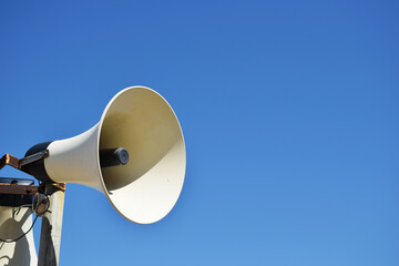 Old weathered vintage public address (PA) megaphone system loudspeaker and blue sky.