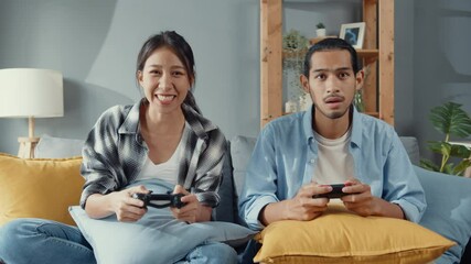 Poster - Happy asia young couple man and woman sit on couch use joystick controller play video game spend fun time together in living room. Asian married couple family lifestyle, Couple stay at home concept.