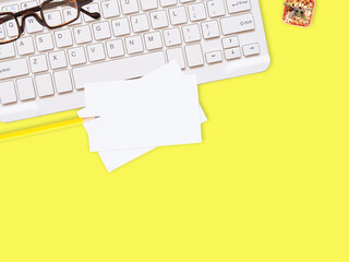 Flat lay white business card over keyboard with glasses, pencil, and cactus on yellow office desktop with copy space for text. Top view.  Business and education concept..