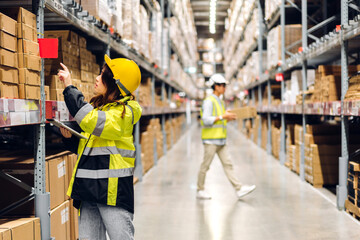 Asian two engineer in helmets team order details on tablet computer for checking goods and supplies on shelves with goods background in warehouse.logistic and business export