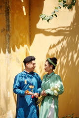 Poster - Beautiful young Veitnamese couple in traditional dresses standing outdoors and lookig at each other