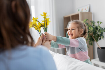 Wall Mural - people, family and holidays concept - happy little daughter giving daffodil flowers to mother at home