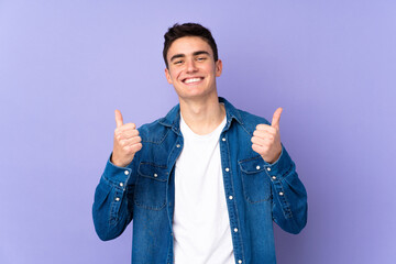 Teenager caucasian  handsome man isolated on purple background with thumbs up gesture and smiling