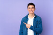 © luismolinero - Teenager caucasian  handsome man isolated on purple background pointing to the side to present a product