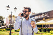 © Mediteraneo - Handsome young man talking on mobile phone, holding coffee to go outdoor.