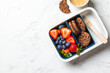 Lunch box with fruits and cookies on white marble background, top view. Takeaway healthy snack container.