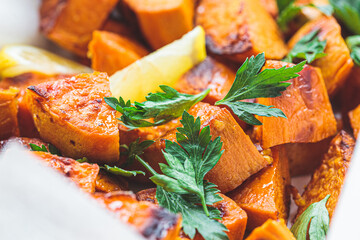 Wall Mural - Close up of baked sweet potato wedges with lemon and parsley in baking dish.