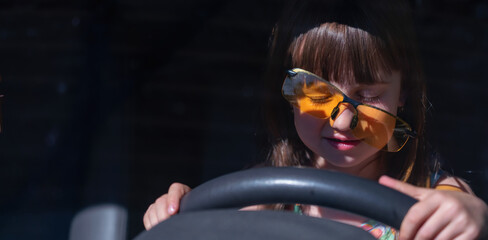 Funny image of little child girl learns to drive a car.