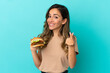 © luismolinero - Young woman holding a burger over isolated background making money gesture