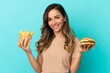 © luismolinero - Young woman holding fried chips  and burger over isolated background